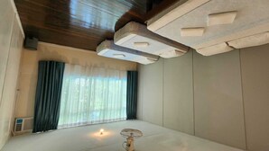 A room with a wooden ceiling, a window with sheer curtains, a standing fan, and a small table with a light. - OYO 90980 Rainbow Island Sepanggar (Sepanggar Island)