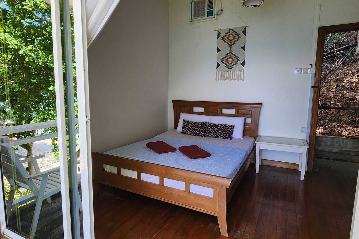 A bedroom with a wooden bed, a small bedside table, and a view of the outdoors.