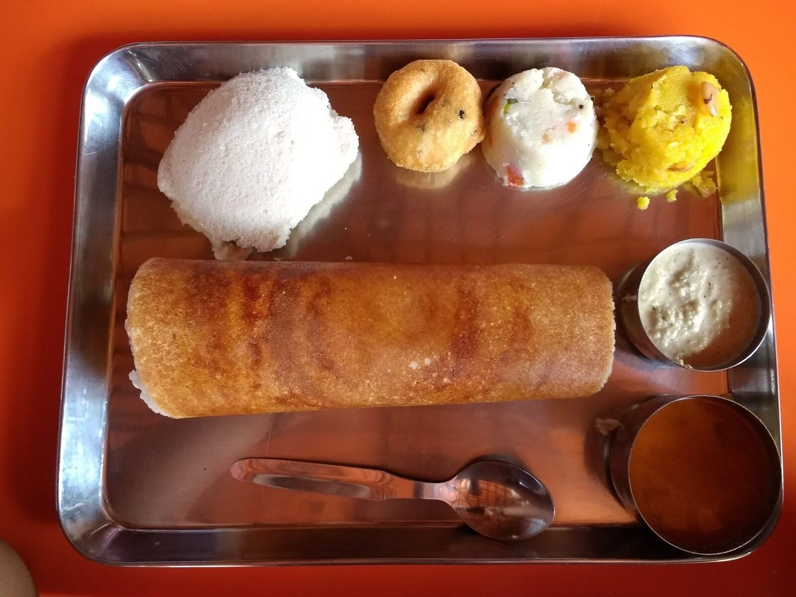 A tray with a variety of Indian snacks including a fried item, a white round item, a yellow item, and two small round items.