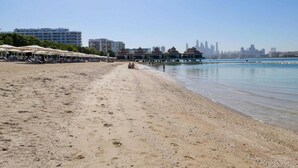 A beach with umbrellas, a pier, and a city skyline in the background. - Luxe 2BR by Dubai Mall Gym/pool by Belvilla (Dubai)