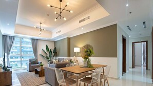 A modern living room with a dining area, large windows, and a view of a building. - Luxe 2BR by Dubai Mall Gym/pool by Belvilla (Dubai)