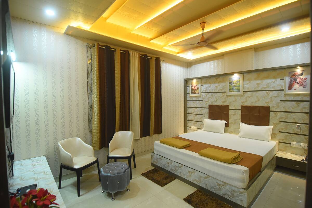 A modern bedroom with a large bed, two chairs, a small ottoman, and a nightstand.