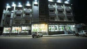 A multi-story hotel with a well-lit entrance, a staircase leading to the entrance, and a parked car in front.