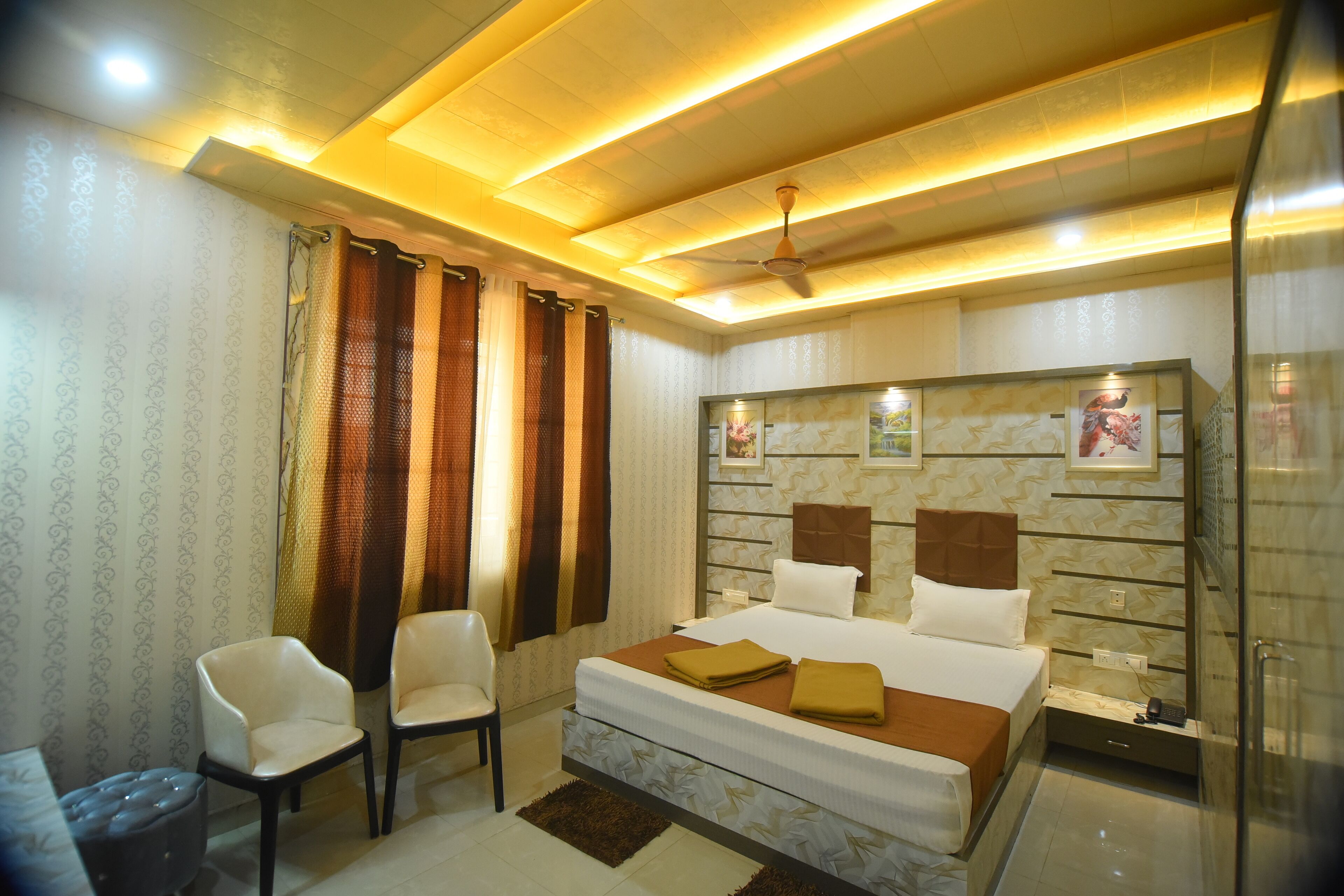 A modern bedroom with a large bed, two chairs, a nightstand, and a ceiling fan.