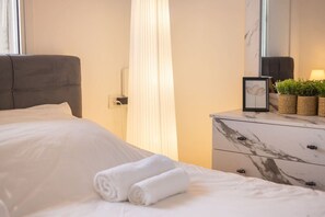 A neatly made bed with white linens and rolled towels, a marble dresser with a mirror, and a small framed picture. - MAMAD - Bahai Gardens Penthouse by Sea N' Rent (Haifa)