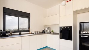A modern kitchen with white cabinets, a black refrigerator, a coffee maker, and a window with a view of the city. - MAMAD - Bahai Gardens Penthouse by Sea N' Rent (Haifa)