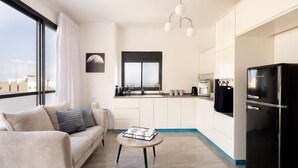 A modern apartment with a sofa, a coffee table, a black refrigerator, and a view of the city through large windows. - MAMAD - Bahai Gardens Penthouse by Sea N' Rent (Haifa)