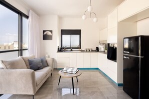 A modern apartment with a sofa, a coffee table, a kitchen with a refrigerator, and a view of the city. - MAMAD - Bahai Gardens Penthouse by Sea N' Rent (Haifa)