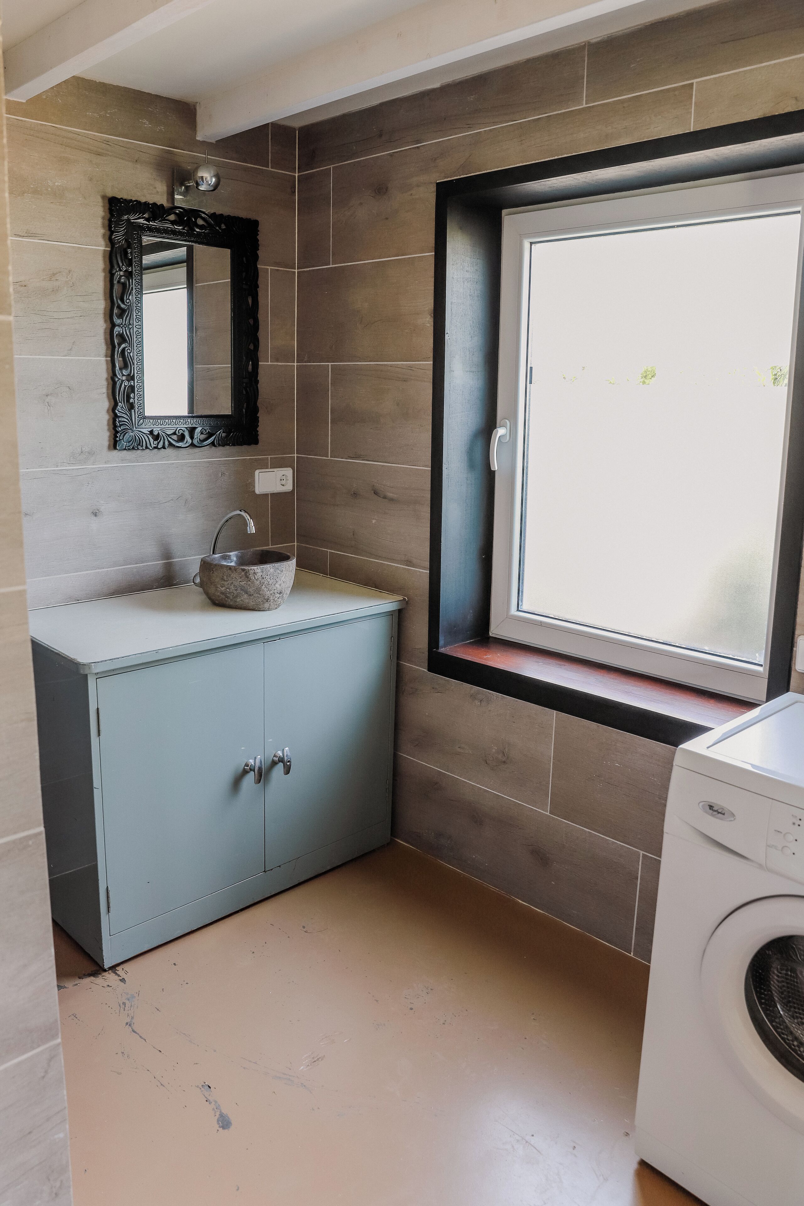 Un baño con un lavamanos de piedra, un espejo, una ventana y una lavadora.