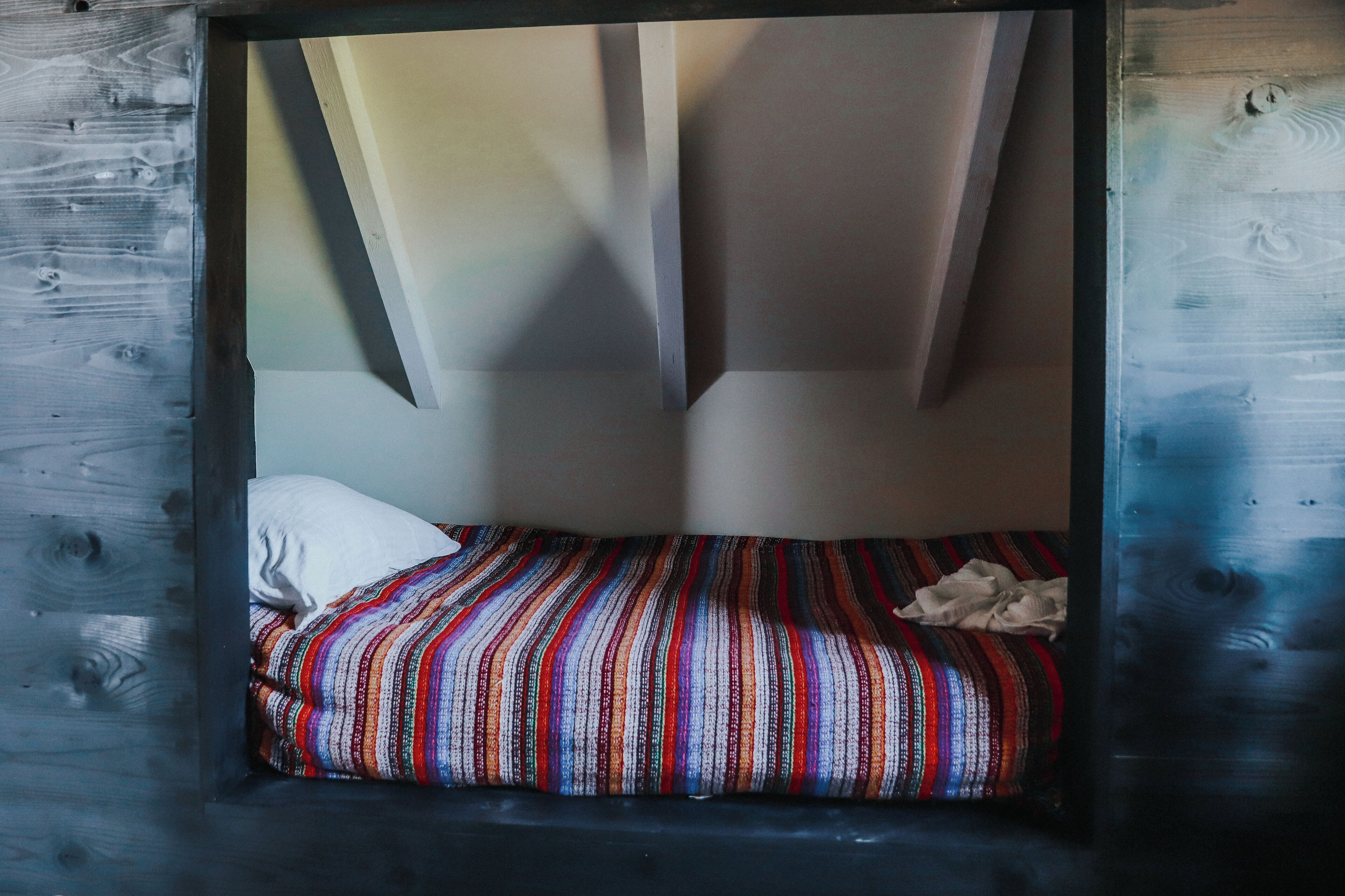 A small, enclosed sleeping area with a single bed, a pillow, and a striped blanket.