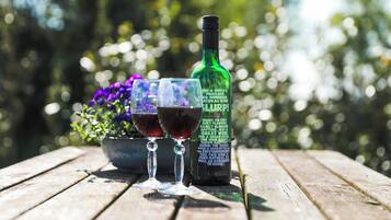 Una botella de vino y dos copas sobre una mesa de madera, con un jardín desenfocado al fondo.