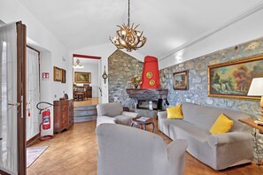 Uma sala de estar com lareira, sofás, um candelabro e uma parede de pedra.