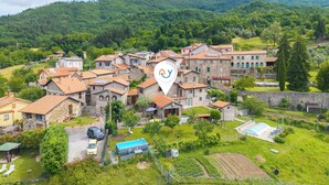 Un borgo con edifici in pietra, una piscina e un'ampia collina sullo sfondo.