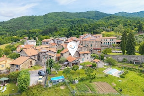 Un village avec des bĂątiments en pierre, une piscine et une grande colline en arriĂšre-plan.