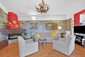 Una sala de estar con chimenea, pared de piedra, sofá gris y televisor.