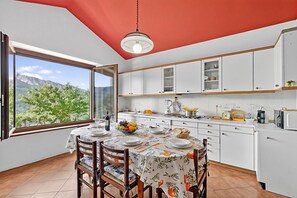 Cozinha moderna com armários brancos, uma mesa de jantar posta para quatro pessoas e uma grande janela com vista para as montanhas.