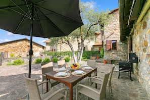 Un edificio de piedra con una mesa en el patio lista para comer, rodeada de sillas de mimbre y una parrilla.