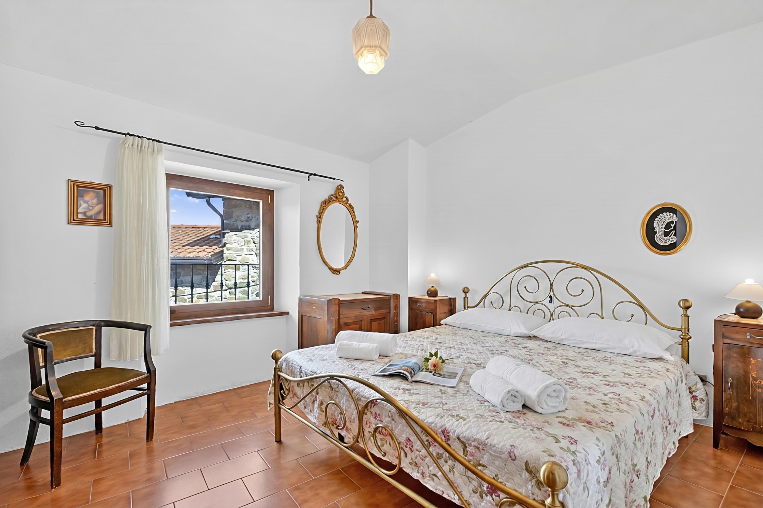 Une chambre à coucher avec un lit, une chaise, une fenêtre, un miroir et une table de chevet.