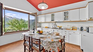Una cucina moderna con mobili bianchi, un tavolo da pranzo per quattro persone e un'ampia finestra con vista sulle montagne.