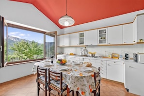 Une cuisine moderne avec des meubles blancs, une table Ă manger pour quatre personnes et une grande fenĂȘtre offrant une vue sur les montagnes.