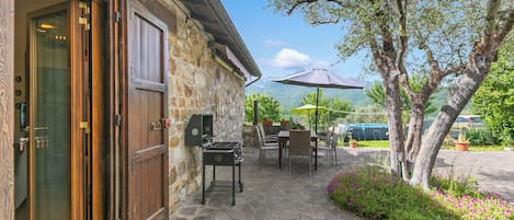 A stone building with a wooden door, outdoor seating, a grill, and a tree with flowers.