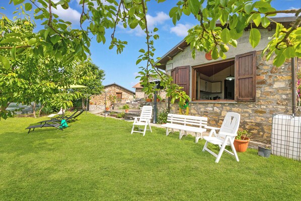 A stone house with a stone wall, a wooden door, and a white bench in the yard.