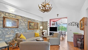 Un soggiorno con parete in pietra, un lampadario, una poltrona, un tavolino da caffè e una televisione sullo sfondo.