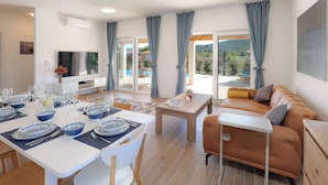 A modern living room with a dining area, a sofa, and a TV. - Papa's court Mediterranean Pasman Villa with pool II (Pasman)