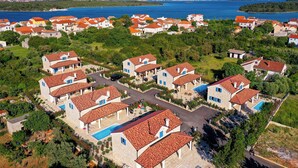 A coastal residential area with houses featuring red-tiled roofs and a central swimming pool. - Papa's court Mediterranean Pasman Villa with pool II (Pasman)
