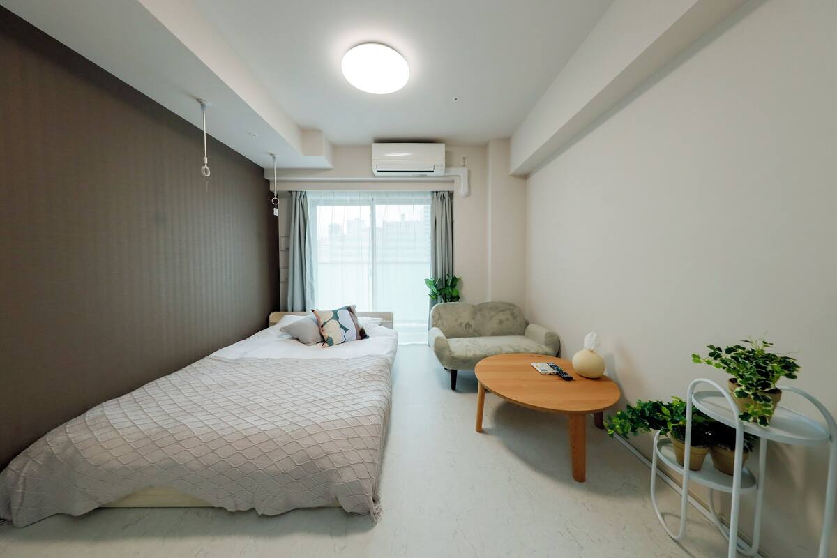 Una habitación de hotel moderna con una cama, un sofá, una mesita y una planta en maceta.