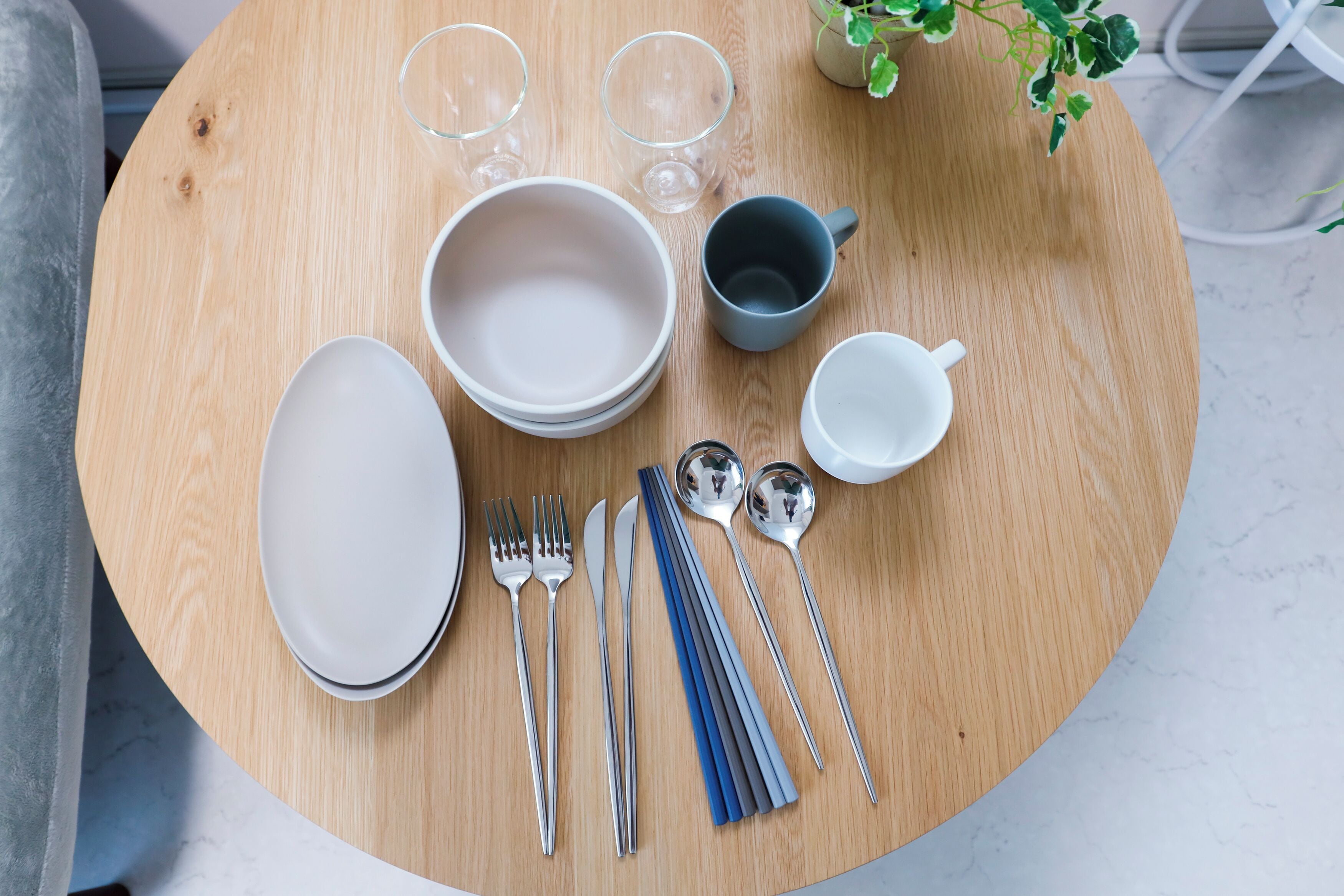 A round wooden table with a set of white plates, bowls, cutlery, and glasses.