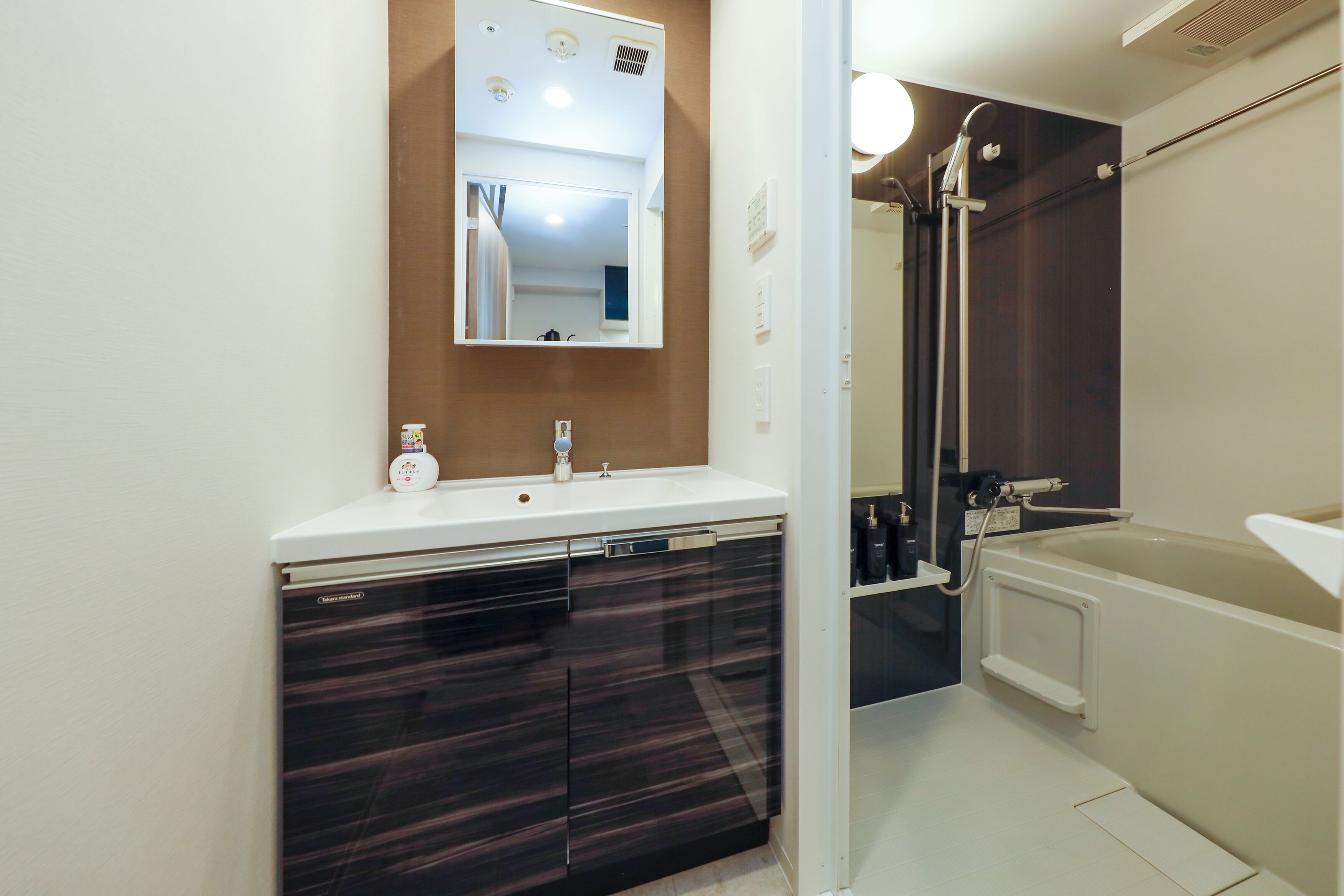 Un bagno moderno con un lavandino bianco, mobili scuri, uno specchio grande e una vasca da bagno.
