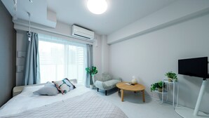 Une chambre d’hôtel moderne avec un grand lit, un petit fauteuil, une table ronde, un téléviseur et une plante en pot.