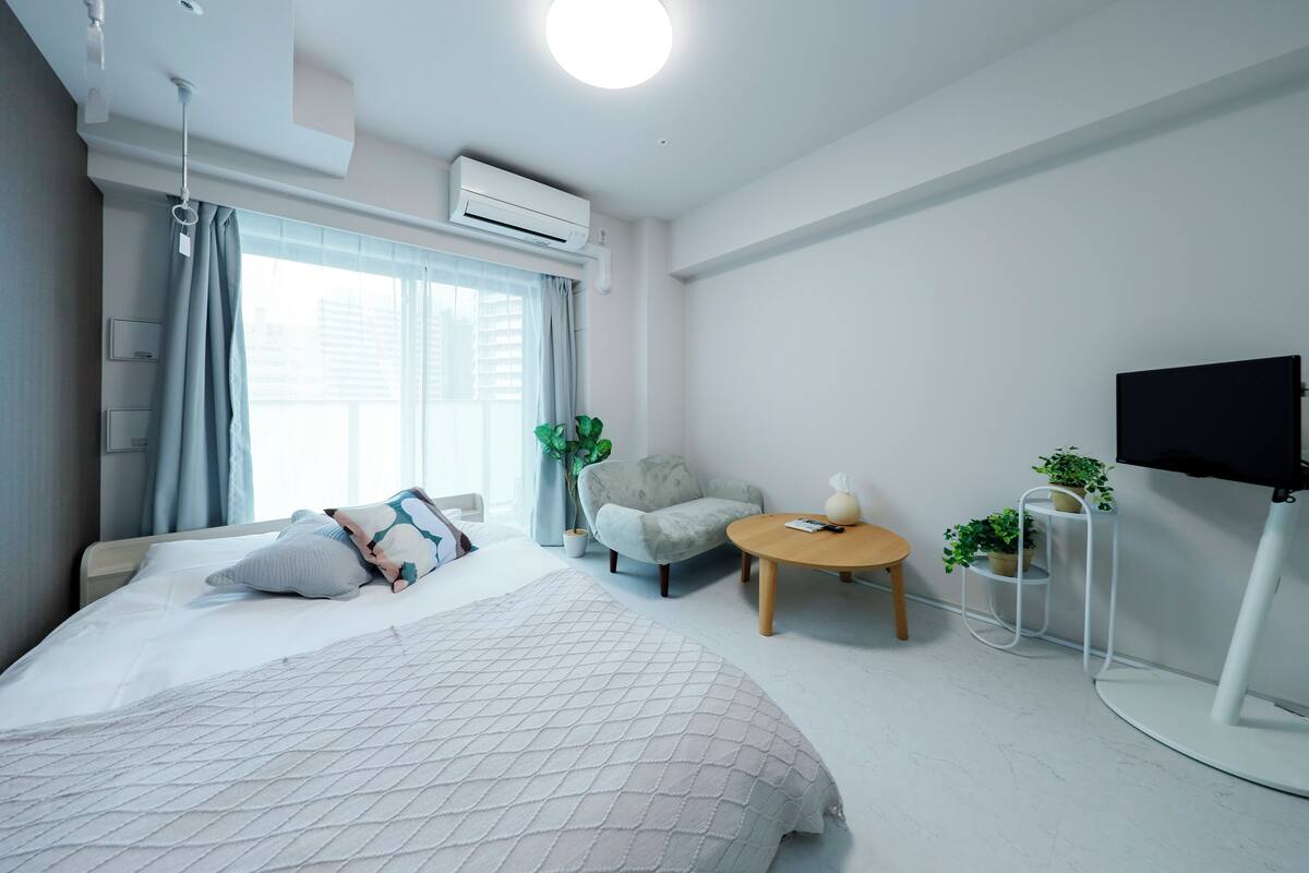Una habitación de hotel moderna con una cama grande, un sillón pequeño, una mesa redonda, un televisor y una planta en maceta.
