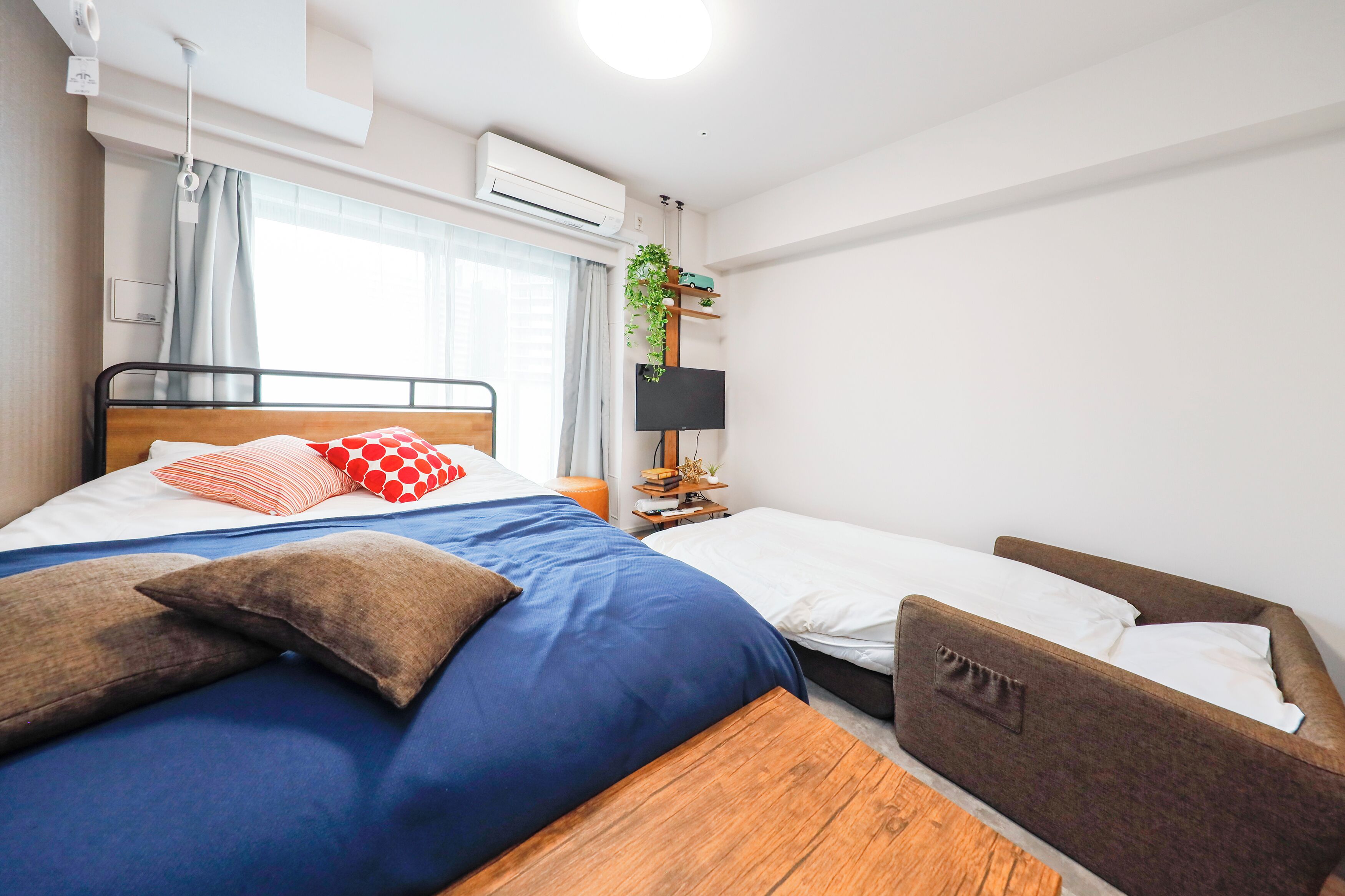 Un dormitorio con cama, mesita de noche, televisor y ventana con cortinas.
