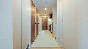 Un couloir étroit et bien éclairé, avec des portes en bois et un sol carrelé, qui mène à une cuisine.