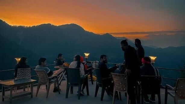 Una terraza con mesas y sillas, con vista a un paisaje montañoso al atardecer.