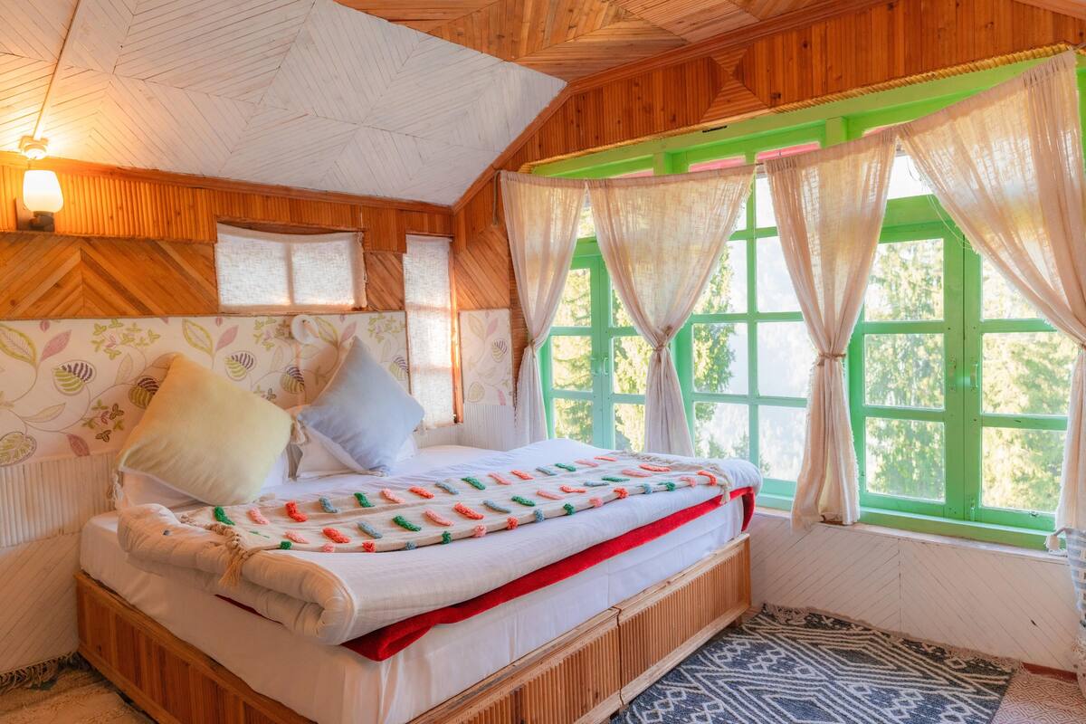 Ein Schlafzimmer in einer Holzhütte mit einem Bett, grünen Fensterrahmen und einer Wand mit Muster.