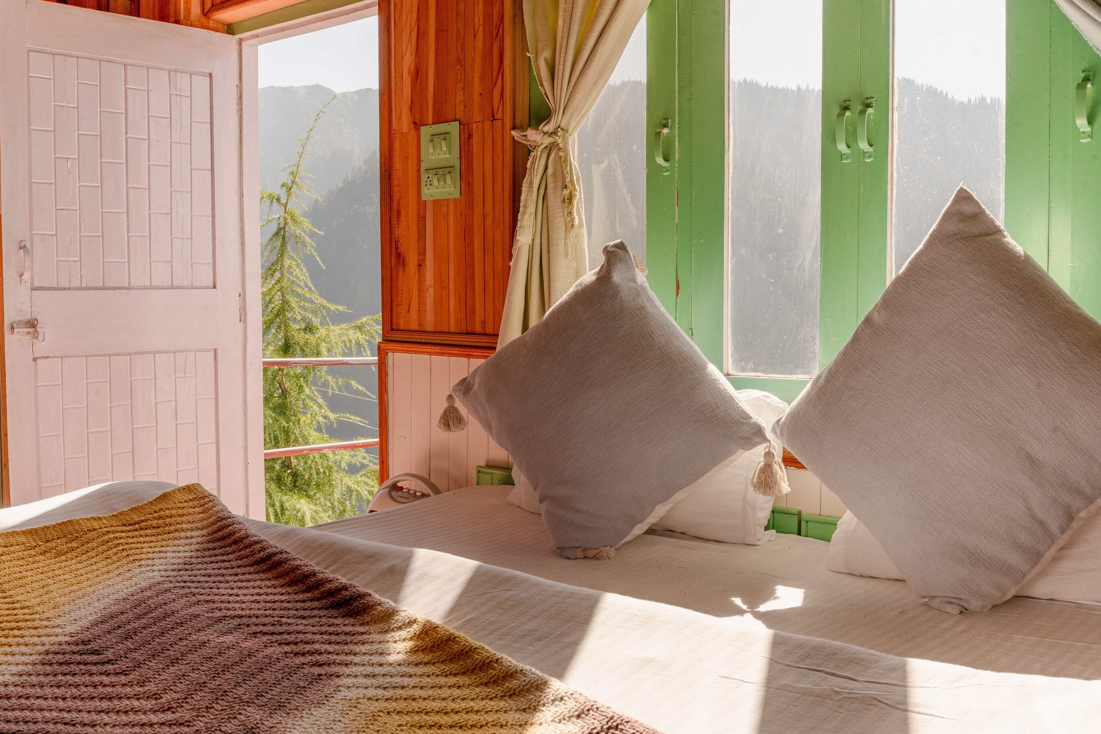 A bedroom with a bed, pillows, a window with a view of mountains, and a door.
