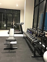 A modern gym with a treadmill, bench press, and a rack of dumbbells.
