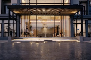 A modern building with large glass windows, a wooden canopy, and a paved entrance area.