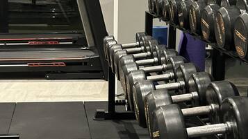 Un gimnasio con una cinta de correr y un estante de mancuernas.