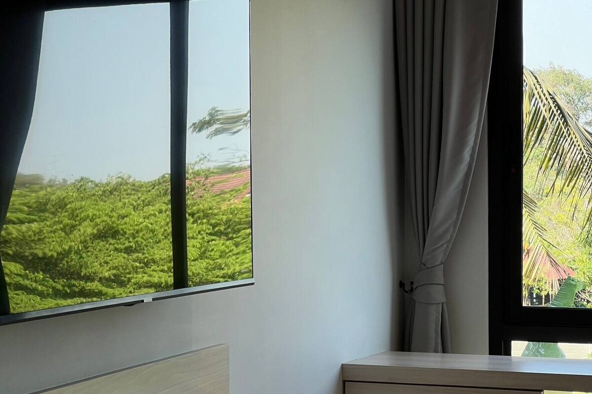 A room with a large window, a flat-screen TV, a wooden shelf, and an air conditioning unit.