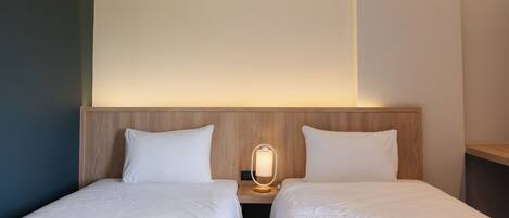 Habitación de hotel con dos camas individuales, cabecera de madera, lámpara de noche y mesita auxiliar.