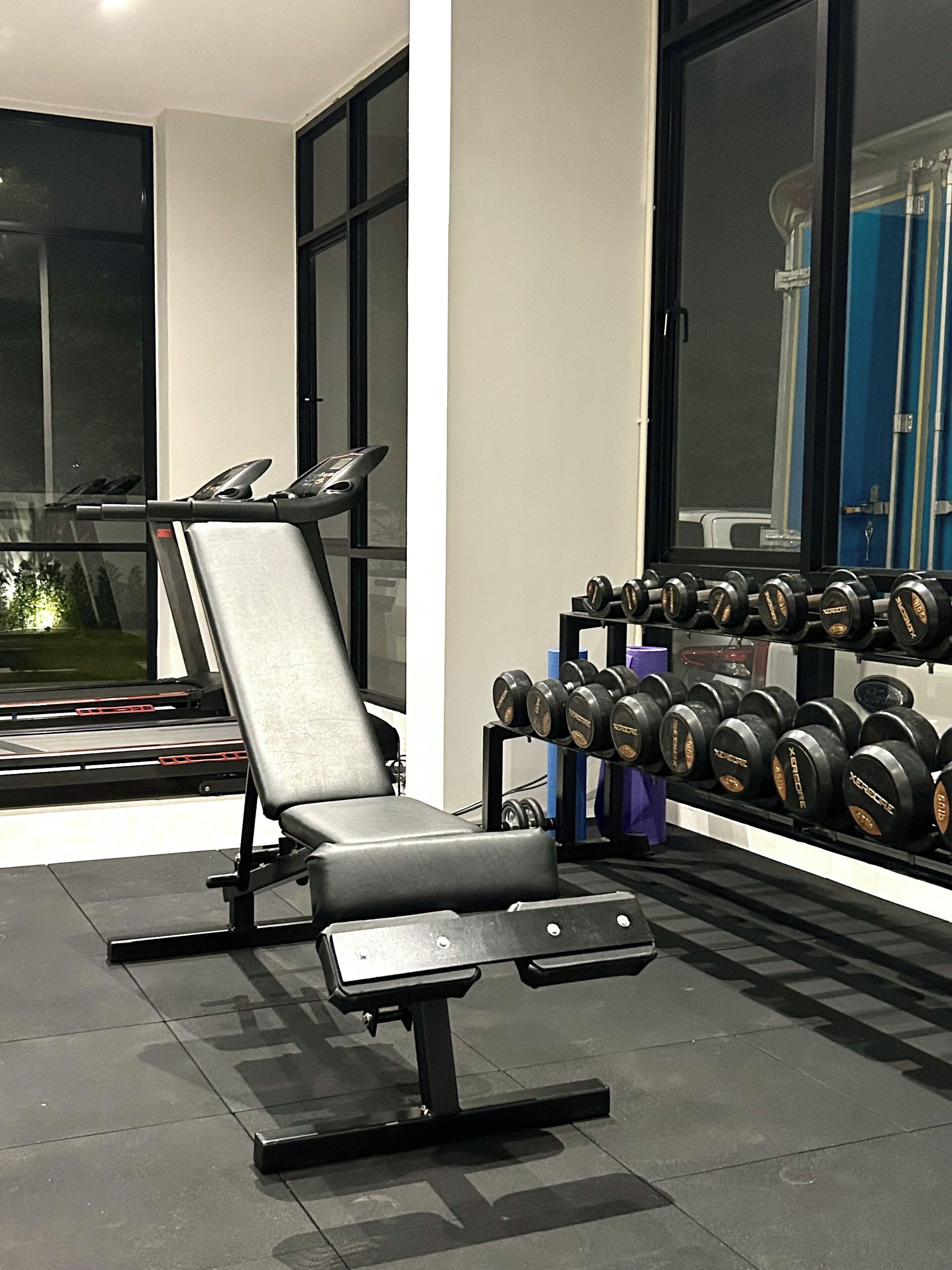 A gym with a bench press, a treadmill, and a rack of dumbbells.