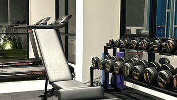 A gym with a bench press, a treadmill, and a rack of dumbbells.