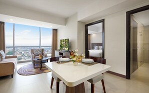 A modern hotel room with a dining area, a large window with a city view, a flat-screen TV, and a bed with a headboard. - Somerset Kencana Jakarta (Jakarta)