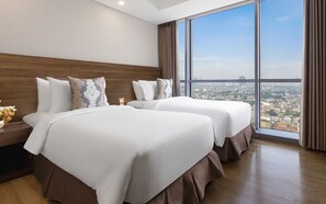 Une chambre d’hôtel avec deux lits, une grande fenêtre donnant sur la ville et une tête de lit en bois.