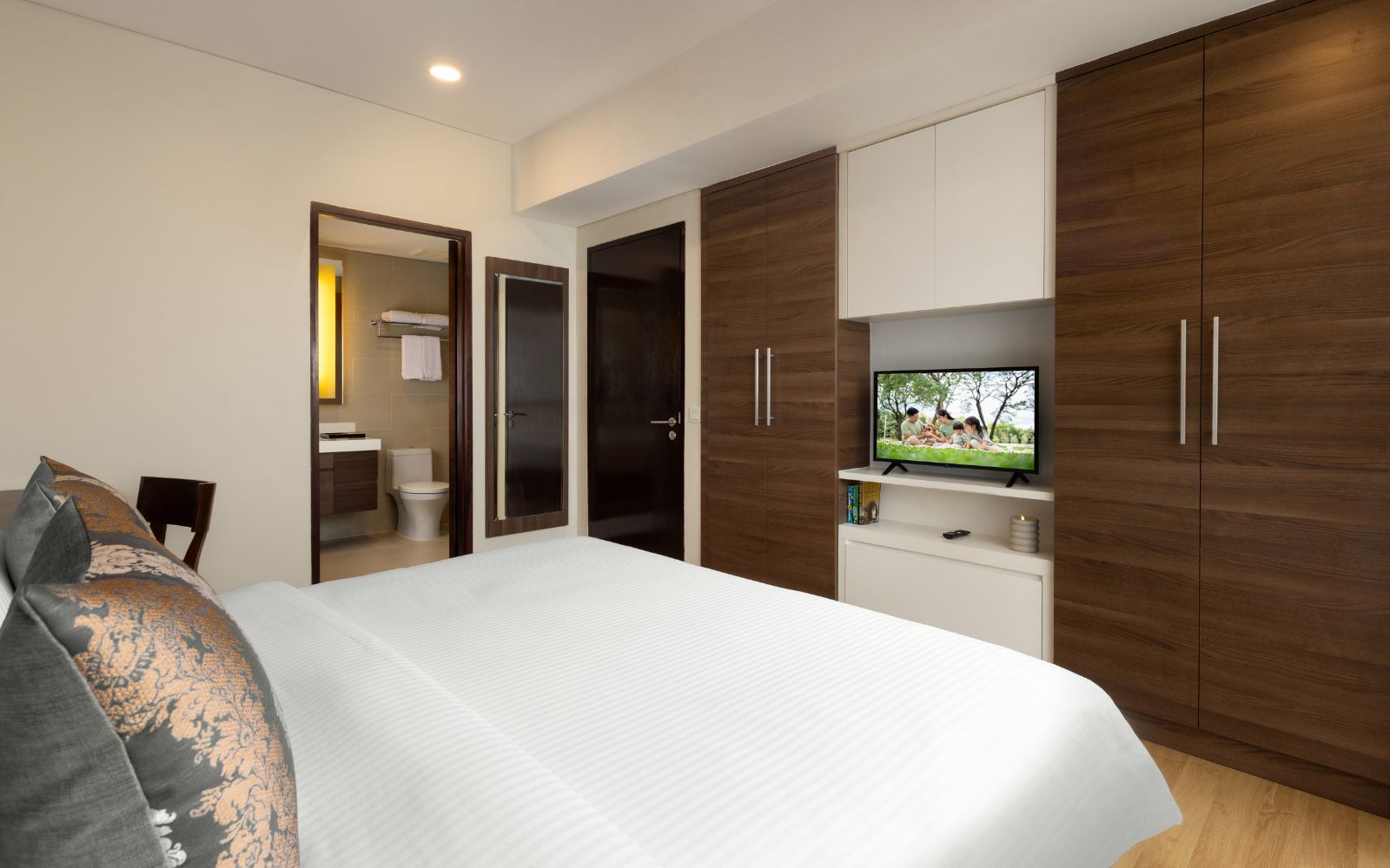 A modern bedroom with a large bed, built-in wardrobe, a television, and a bathroom visible through an open door.