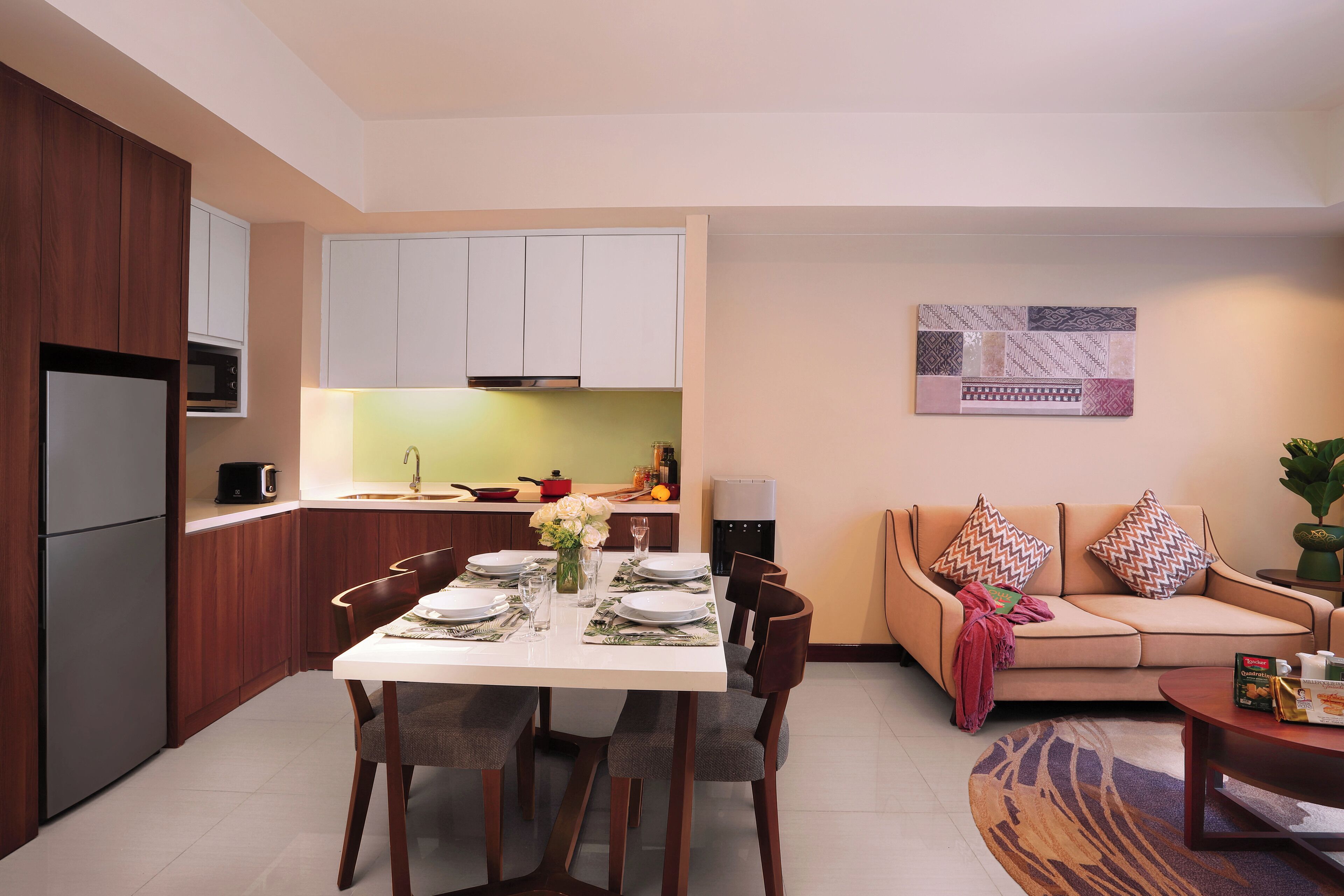 A modern kitchen with white cabinets, a dining table set for four, and a sofa in the living area.